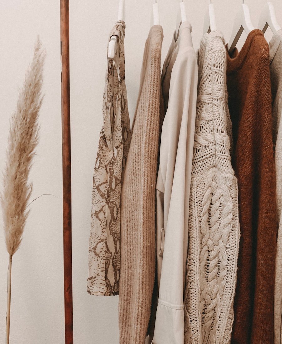 Rail of beige and cream knitwear beside dried pampas grass in a bright studio