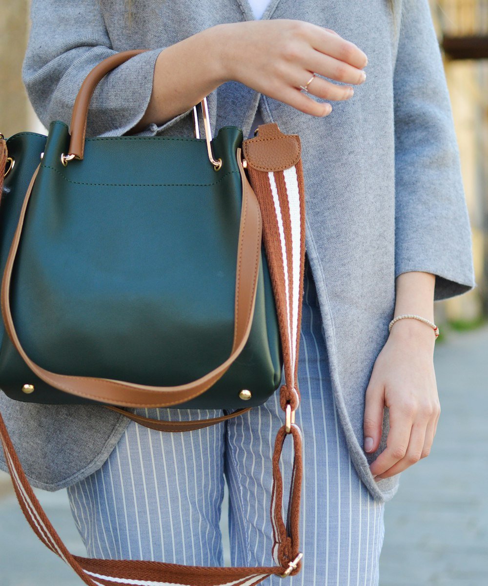 Woman in a grey coat carrying a dark green handbag over her shoulder on a street